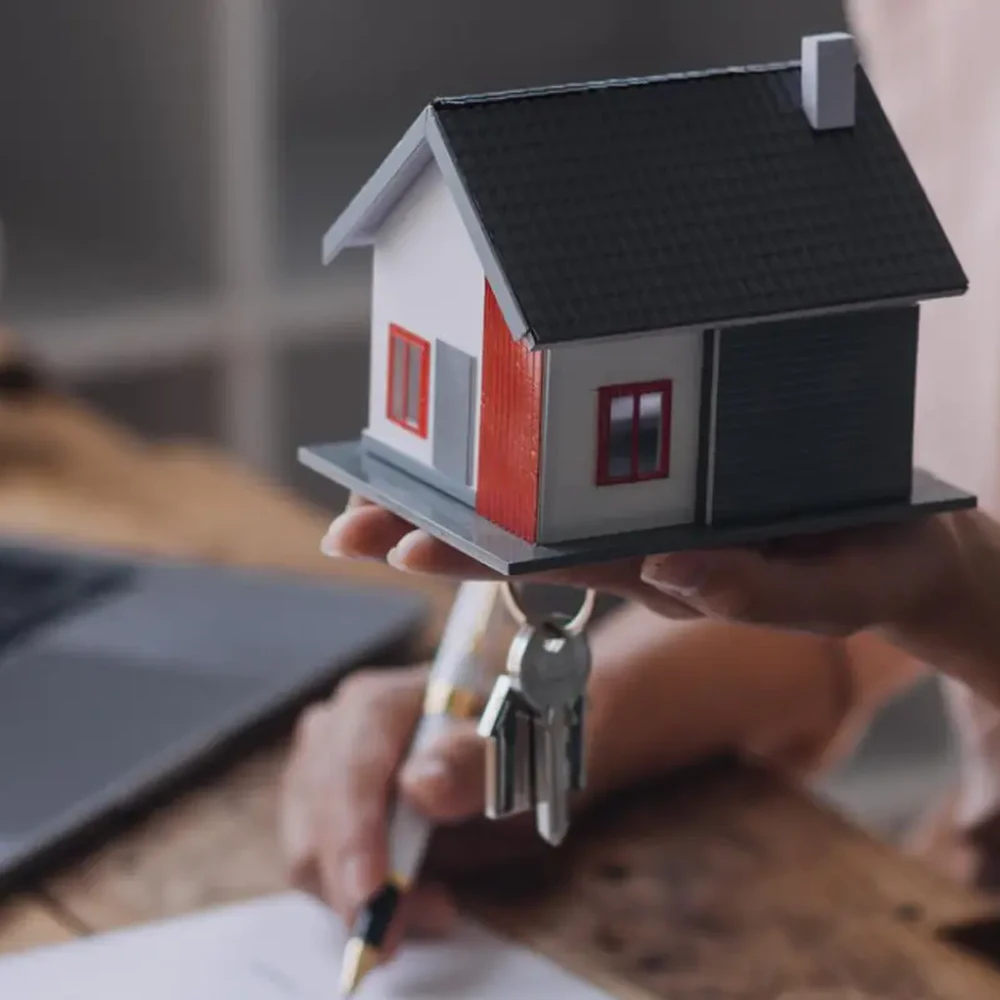 Mano che regge una casa in miniatura con le chiavi accanto a un laptop